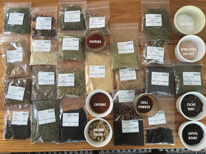May include: A collection of spices and ingredients in clear plastic bags and small bowls. The ingredients include paprika, cayenne pepper, chili powder, brown sugar, table salt, Himalayan sea salt, cocoa nibs, and coffee beans. The labels on the bags indicate the names of the spices and ingredients.
