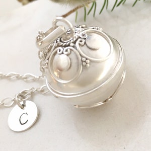 May include: Silver charm necklace featuring a round, ornate pendant and a small disc charm engraved with the letter 'C'.