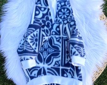 May include: A navy blue and white patterned fleece hoodie with a hood and white cuffs and hem. The hoodie features a geometric floral design. The garment is displayed on a white fluffy surface.