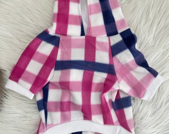 May include: A pink, white, and navy blue plaid dog hoodie with a hood and short sleeves. The hoodie has a white trim on the hood, sleeves, and bottom hem. The garment is made of a soft, fleece-like material.