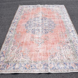 May include: A large, rectangular rug with a distressed, vintage appearance. The rug features a central medallion design in shades of blue and white against a faded coral background. The border is a darker blue with intricate floral patterns.