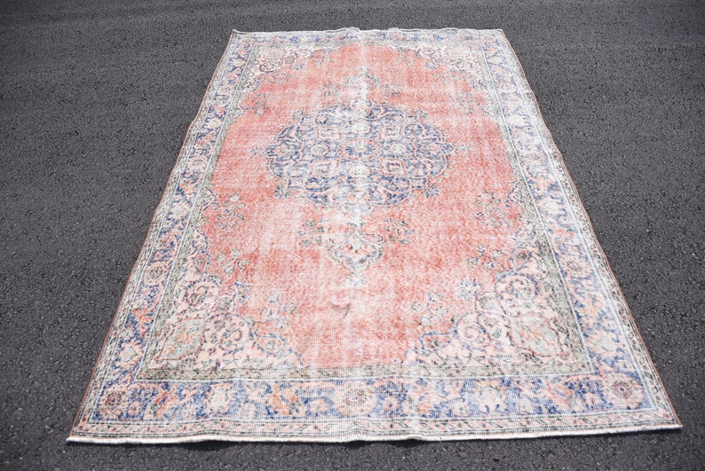 May include: A large, rectangular rug with a distressed, vintage appearance. The rug features a central medallion design in shades of blue and white against a faded coral background. The border is a darker blue with intricate floral patterns.