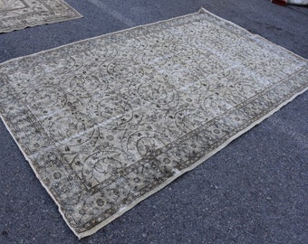 May include: A large, off-white rug with a floral pattern in a darker shade of brown. The rug has a border with a repeating pattern.