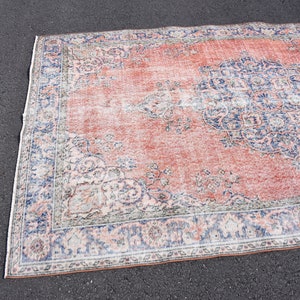 May include: A rectangular rug with a distressed appearance, featuring a faded red central area and detailed blue and white floral patterns. The rug has a border with similar blue and white designs. Ideal for living rooms and bedrooms.