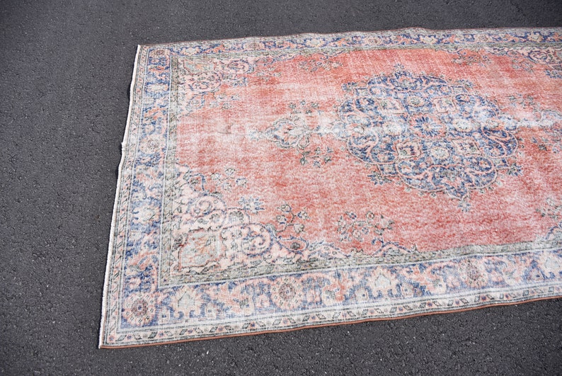 May include: A rectangular rug with a distressed appearance, featuring a faded red central area and detailed blue and white floral patterns. The rug has a border with similar blue and white designs. Ideal for living rooms and bedrooms.