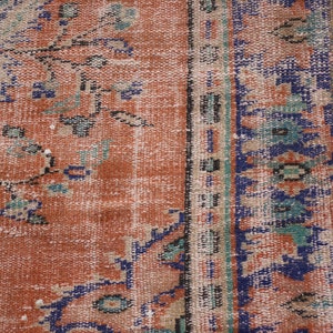 May include: Close-up of a vintage rug with a faded orange background and a blue and green floral pattern. The rug has a fringe border.