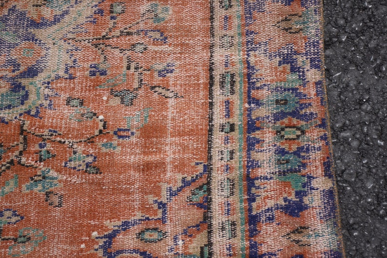May include: Close-up of a vintage rug with a faded orange background and a blue and green floral pattern. The rug has a fringe border.