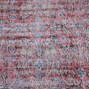 May include: Close-up of a vintage rug with a distressed, faded appearance. The rug features a complex pattern in shades of red, white, blue, and black. The design includes floral and geometric elements, creating a textured, antique look.