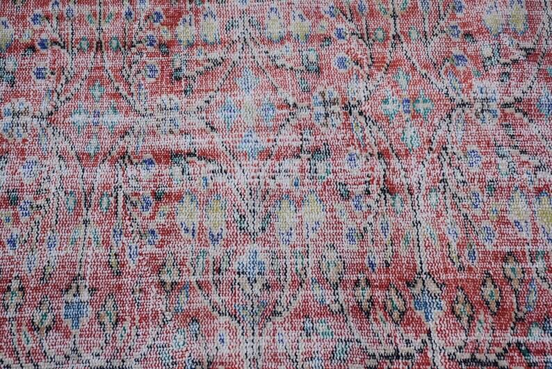 May include: Close-up of a vintage rug with a distressed, faded appearance. The rug features a complex pattern in shades of red, white, blue, and black. The design includes floral and geometric elements, creating a textured, antique look.