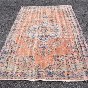 May include: A vintage rug with a faded peach background and a floral pattern in shades of blue, green, and pink. The rug has a distressed look and a fringed edge.