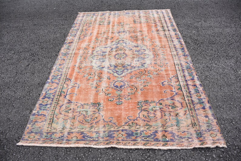 May include: A vintage rug with a faded peach background and a floral pattern in shades of blue, green, and pink. The rug has a distressed look and a fringed edge.