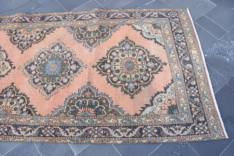 May include: A vintage rug with a peach background and intricate floral patterns in shades of blue, green, and black. The rug has a dark brown border with a repeating pattern.