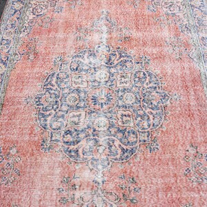 May include: A distressed, rectangular rug with a central medallion design. The rug has a faded, vintage aesthetic with a coral-red field and a navy blue and cream border and medallion. The rug's dimensions are not visible.