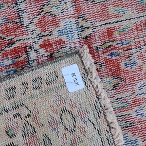 May include: Close-up of a section of a vintage rug with a distressed, woven design. The rug features a red and cream color palette with accents of blue and green. The label reads "OC 11631".