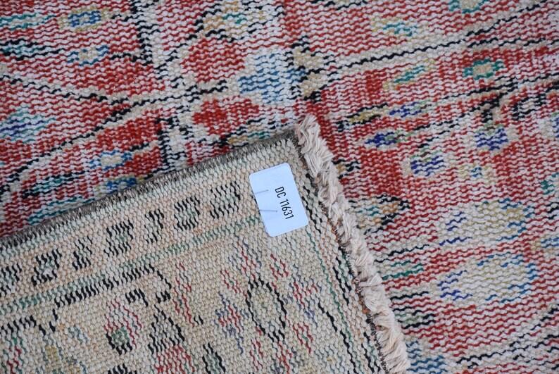May include: Close-up of a section of a vintage rug with a distressed, woven design. The rug features a red and cream color palette with accents of blue and green. The label reads "OC 11631".