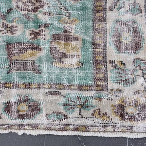 May include: Close-up of a distressed, vintage rug with a faded, floral pattern. The rug features a teal, beige, and brown color palette. The design includes floral and geometric elements, with a fringed edge.
