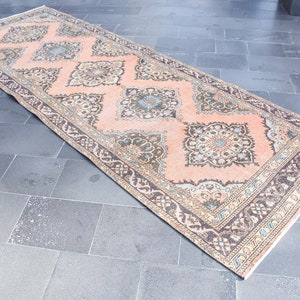 May include: A vintage runner rug with a peach background and intricate floral patterns in shades of brown, beige, and blue. The rug has a fringed edge.