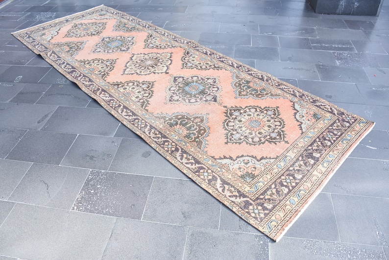 May include: A vintage runner rug with a peach background and intricate floral patterns in shades of brown, beige, and blue. The rug has a fringed edge.
