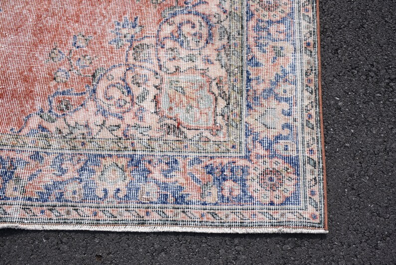 May include: A fragment of a vintage rug with a faded, distressed look. The rug displays a central field of muted coral with detailed floral patterns in blue, cream, and green. A detailed border frames the design.