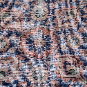 May include: Close-up of a vintage rug with an intricate floral pattern. The rug features a dark blue background with a repeating design in shades of red, beige, and green. The detailed pattern creates a textured appearance.