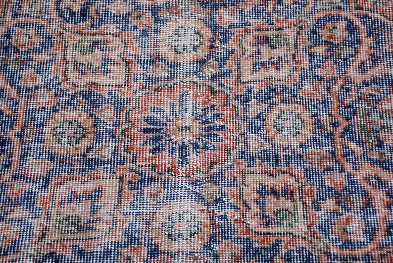 May include: Close-up of a vintage rug with an intricate floral pattern. The rug features a dark blue background with a repeating design in shades of red, beige, and green. The detailed pattern creates a textured appearance.