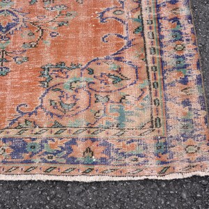 May include: Close-up of a vintage rug with a faded orange background and a blue and green floral pattern. The rug has a fringed edge.