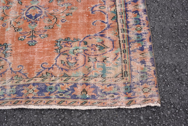 May include: Close-up of a vintage rug with a faded orange background and a blue and green floral pattern. The rug has a fringed edge.