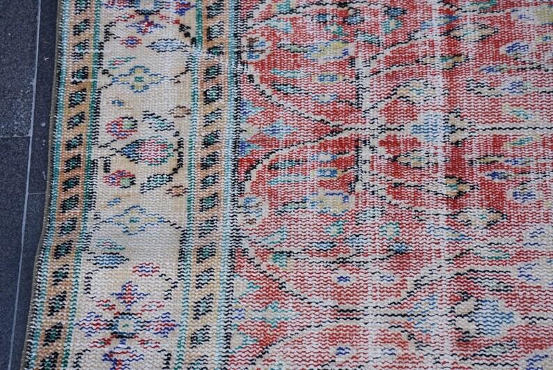 May include: Close-up of a section of a vintage rug with a distressed, faded appearance. The rug features a complex pattern in shades of red, beige, blue, and green. The design includes floral and geometric elements, with a black border.