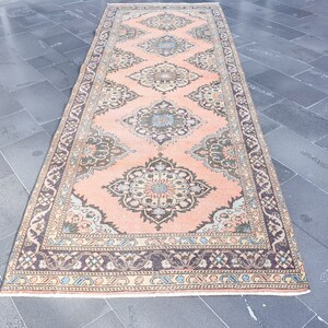May include: A vintage runner rug with a peach background and intricate floral patterns in shades of brown, blue, and cream. The rug has a border with a repeating pattern of brown, cream, and blue.