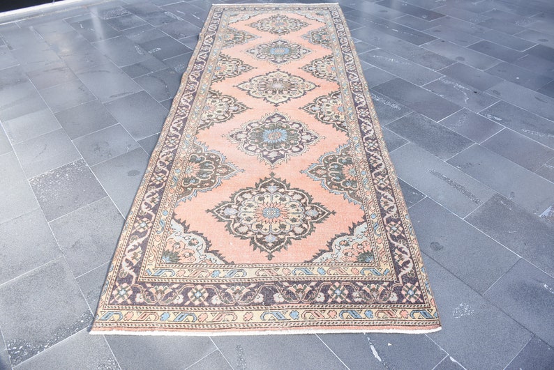 May include: A vintage runner rug with a peach background and intricate floral patterns in shades of brown, blue, and cream. The rug has a border with a repeating pattern of brown, cream, and blue.