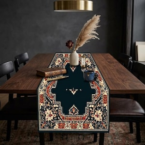 May include: A dark teal table runner with an intricate, ornate pattern in shades of red, beige, and black. The runner is placed on a dark wood dining table, with a vase of dried flowers and a book on top.