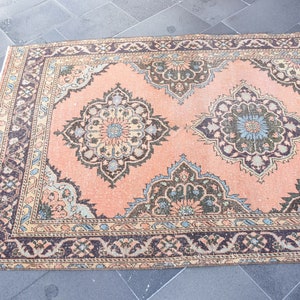 May include: A vintage peach-colored rug with a floral pattern in shades of brown, blue, and cream. The rug has a border with a repeating design.