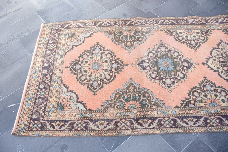 May include: A vintage peach-colored rug with a floral pattern in shades of brown, blue, and cream. The rug has a border with a repeating design.