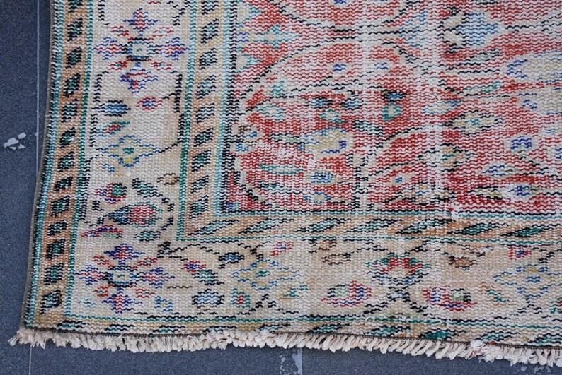 May include: Close-up of a section of a vintage rug with a distressed appearance. The rug features a central field of red and cream hues, with intricate floral patterns in blue, green, and black. The border is cream with floral motifs and a fringed edge.