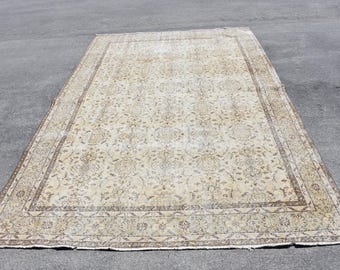 Op de afbeelding: Een vintage crèmekleurig tapijt met een bloemenpatroon en een bruine rand. Het tapijt heeft een verweerde uitstraling en is gemaakt van wol.