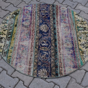 Puede incluir: Alfombra redonda de estilo vintage con diseño patchwork. Presenta un panel central azul marino con motivos florales, flanqueado por rayas verticales rosas, azules y beige. Los bordes tienen un borde verde. Diámetro: aprox. 120 cm.