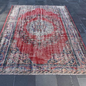 May include: A vintage red and blue rug with a faded floral pattern. The rug has a distressed look and is made of wool.