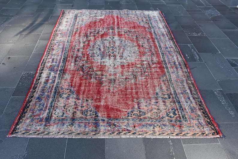 May include: A vintage red and blue rug with a faded floral pattern. The rug has a distressed look and is made of wool.