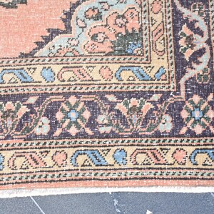 May include: Close-up of the bottom edge of a vintage rug with a floral pattern in shades of pink, blue, and green. The rug has a dark brown border with a geometric design.