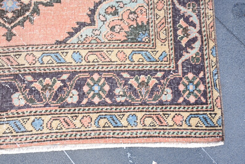 May include: Close-up of the bottom edge of a vintage rug with a floral pattern in shades of pink, blue, and green. The rug has a dark brown border with a geometric design.