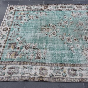 May include: A distressed, rectangular rug with a faded turquoise field and a detailed border. The rug features floral and geometric patterns in shades of brown, beige, and gold. The rug is likely made of wool and is suitable for a living room or bedroom.