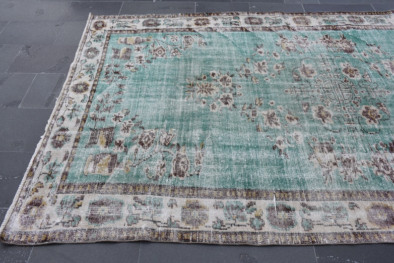 May include: A distressed, rectangular rug with a faded turquoise field and a detailed border. The rug features floral and geometric patterns in shades of brown, beige, and gold. The rug is likely made of wool and is suitable for a living room or bedroom.