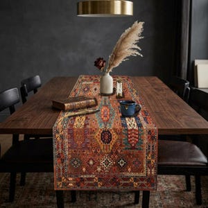 Könnte beinhalten: Ein rechteckiger Tischläufer mit traditionellem Teppichdesign in Rot-, Orange-, Blau- und Beigetönen. Der Läufer liegt auf einem dunklen Holztisch, mit einer Vase, einem Buch und einer Tasse darauf. Der Tisch ist von schwarzen Stühlen umgeben.