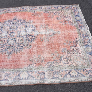 May include: A rectangular rug with a distressed, vintage appearance. The rug has a coral-red central field with faded blue and cream floral patterns. The border is a darker blue with similar detailing. The rug's style suggests a traditional design.