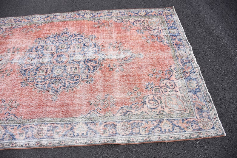 May include: A rectangular rug with a distressed, vintage appearance. The rug has a coral-red central field with faded blue and cream floral patterns. The border is a darker blue with similar detailing. The rug's style suggests a traditional design.