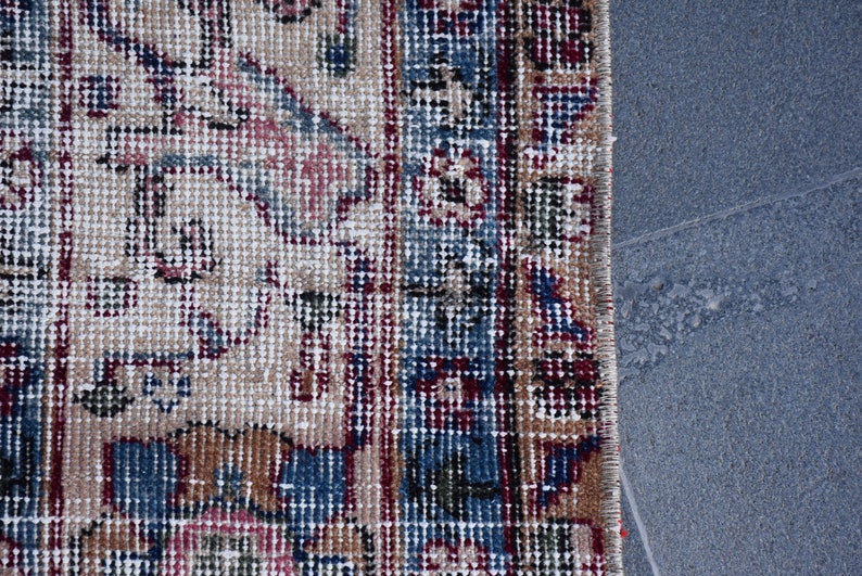 Puede incluir: Primer plano del borde de una alfombra con un patr&oacute;n detallado en tonos de azul, rojo y beige. La alfombra est&aacute; tejida con una textura fina y tiene flecos a lo largo del borde.