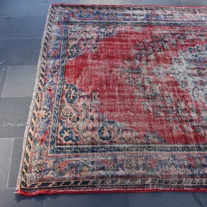 May include: A vintage red and blue rug with a faded floral pattern. The rug has a distressed look and is made of wool.