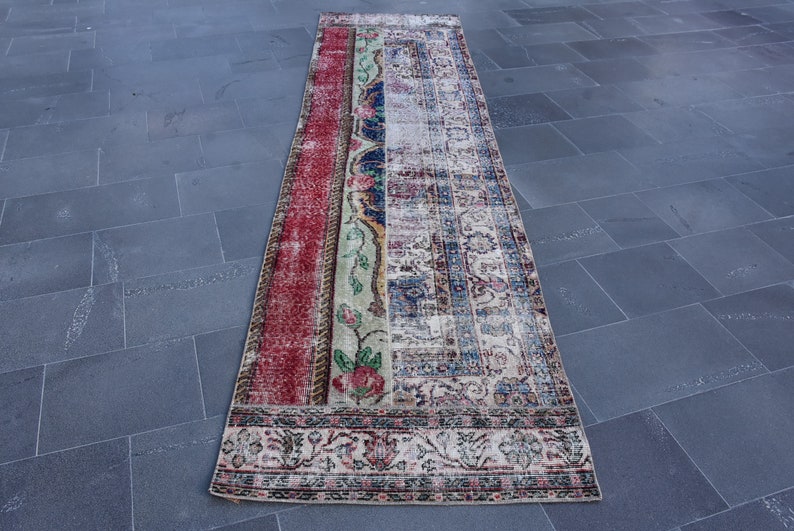 Puede incluir: Una alfombra de pasillo vintage con un dise&ntilde;o de patchwork en rojo, azul, verde y crema. La alfombra tiene un patr&oacute;n floral y un borde con un dise&ntilde;o repetitivo.
