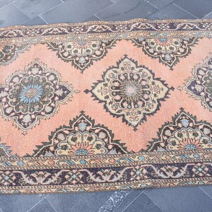 May include: A vintage pink rug with a floral pattern in shades of green, blue, and beige. The rug has a dark brown border with a geometric design.