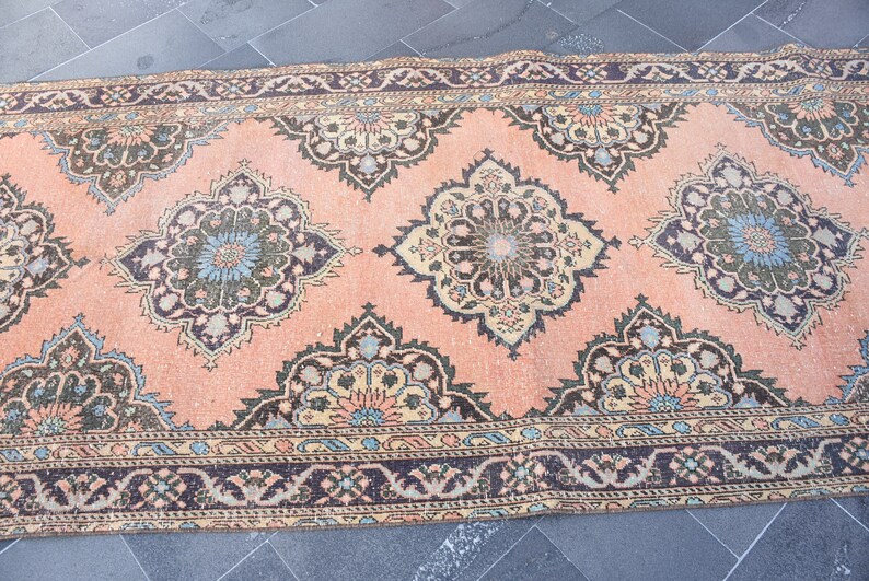 May include: A vintage pink rug with a floral pattern in shades of green, blue, and beige. The rug has a dark brown border with a geometric design.